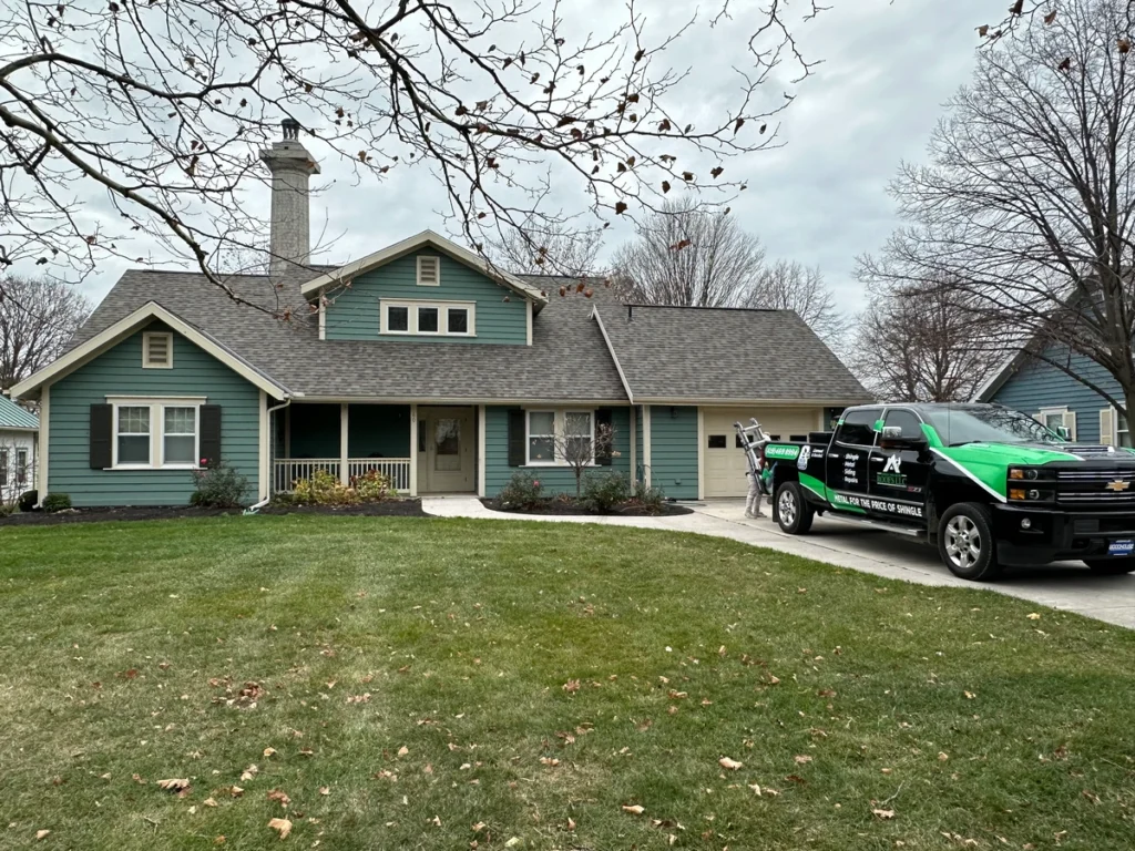 Outdoor view of a home with green siding and a new roof replacement with shingle and metal truck outside
