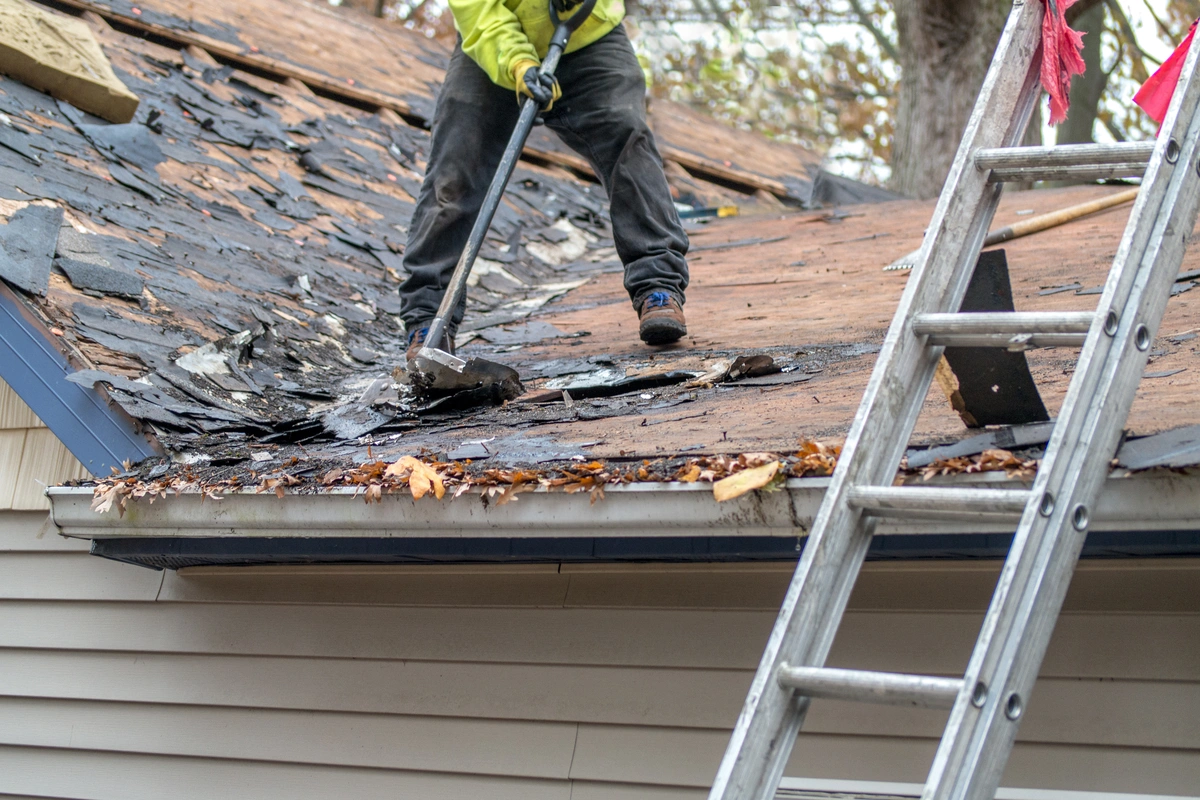 construction worker removing the asphalt shingles from the house roof