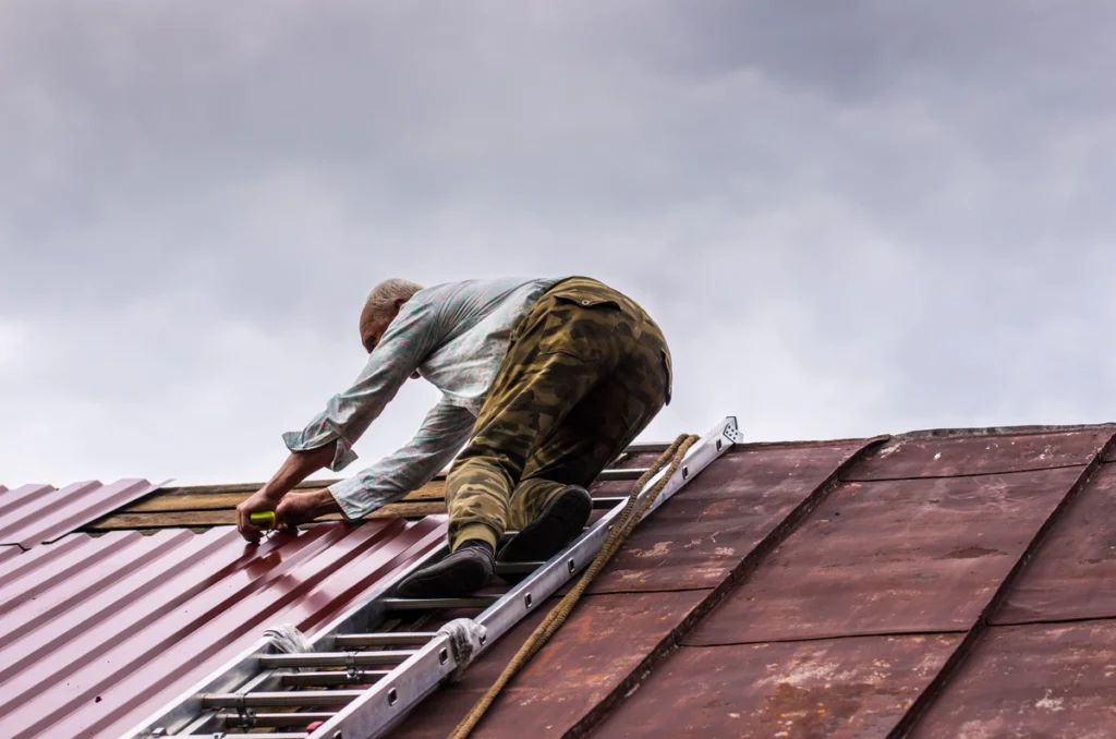 man repairing the metal roof dents standing on stairs