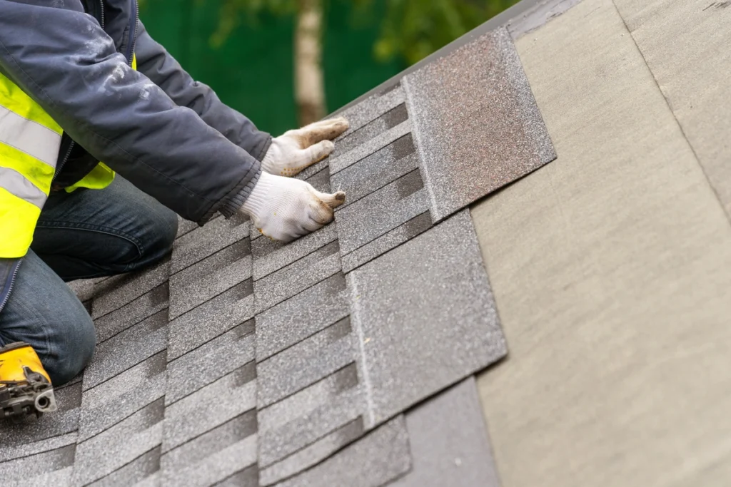 roofer installing brand new asphalt shingles on house roof