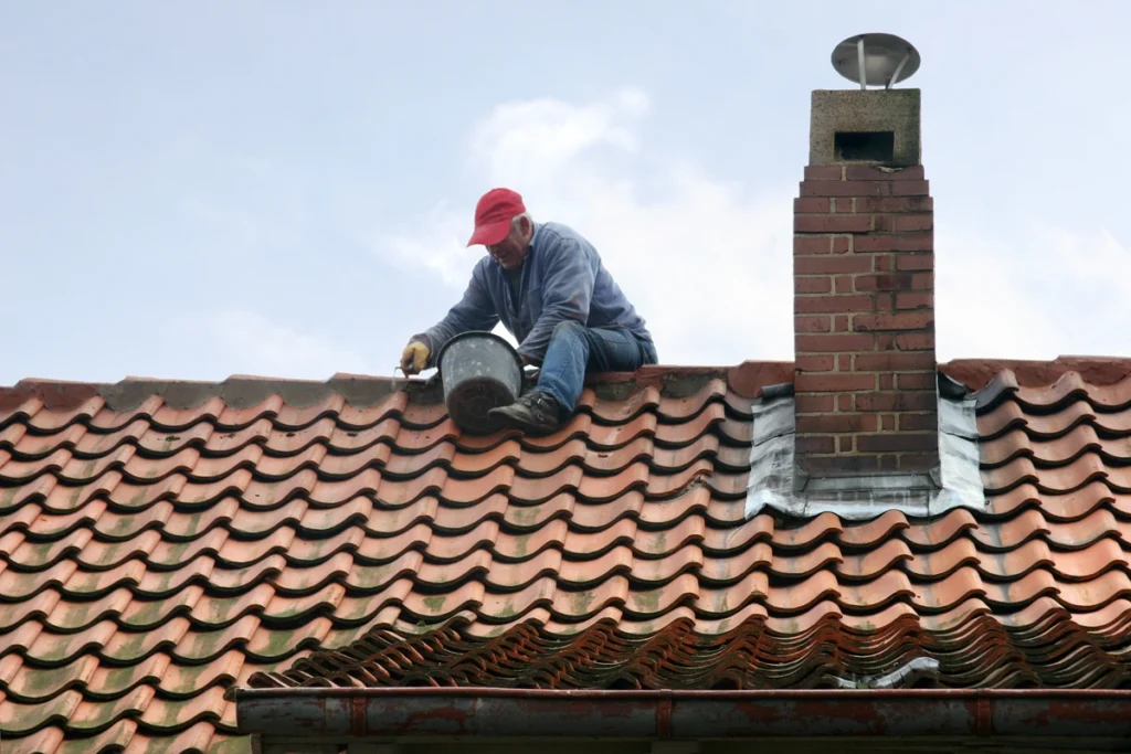 worker repairing and preventing damage on roof filling cement between tiles