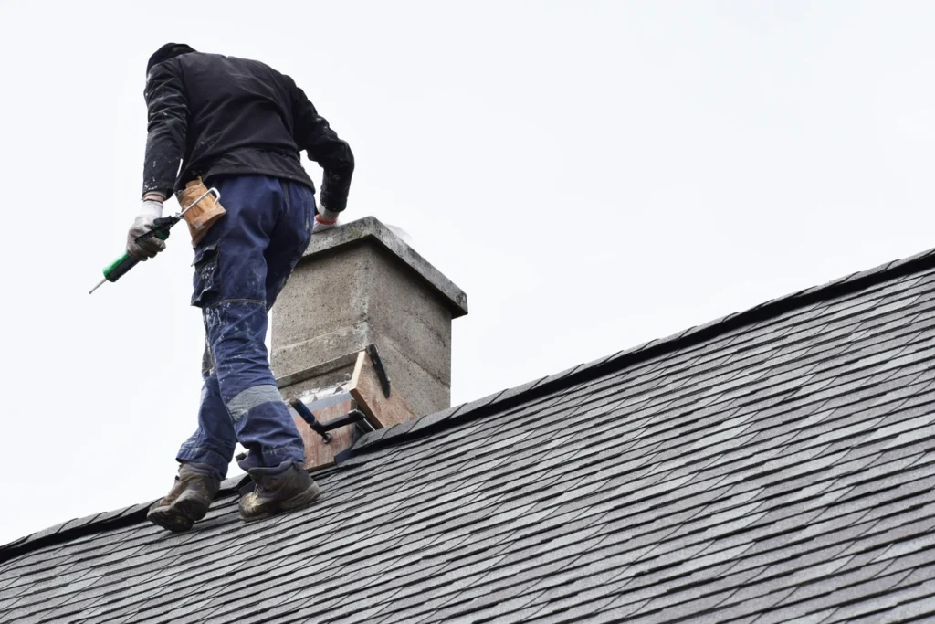 A man with roofing tools is walking on an asphalt shingle roof
