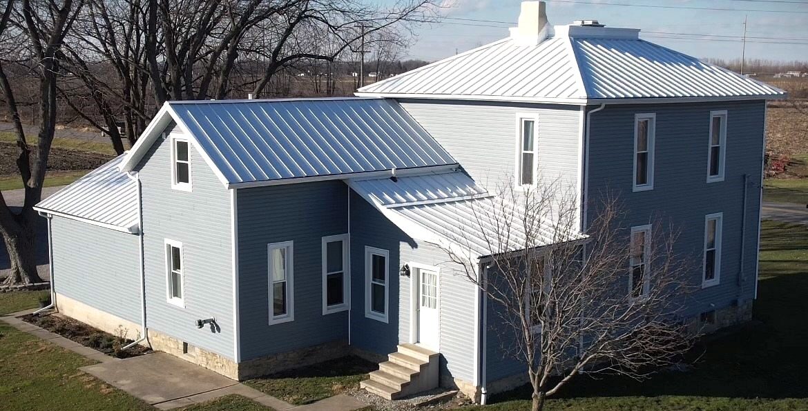 Sun capturing beautifully installed blue vinyl siding, custom double hung windows and polar white metal roofing.