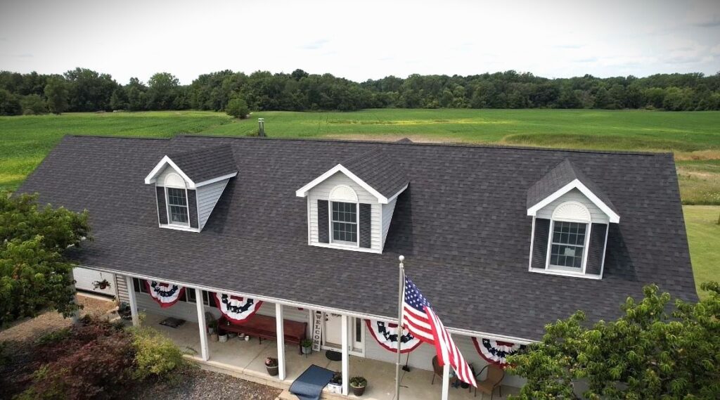 Owens Corning Onyx Black asphalt shingle roofing replacement with American flag in foreground and country land in background.