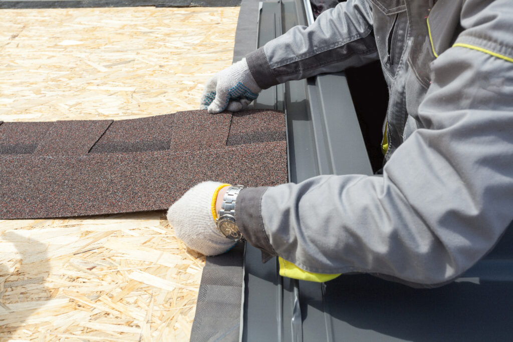 A man placing shingles on the roof, securing them for weather protection and structural integrity.